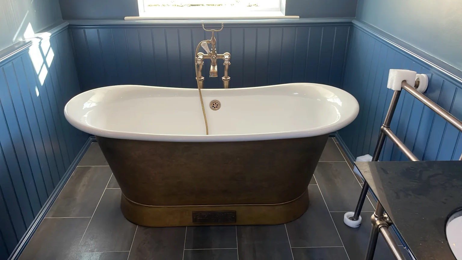 Brass-coloured freestanding bath framed by rich blue wall panelling