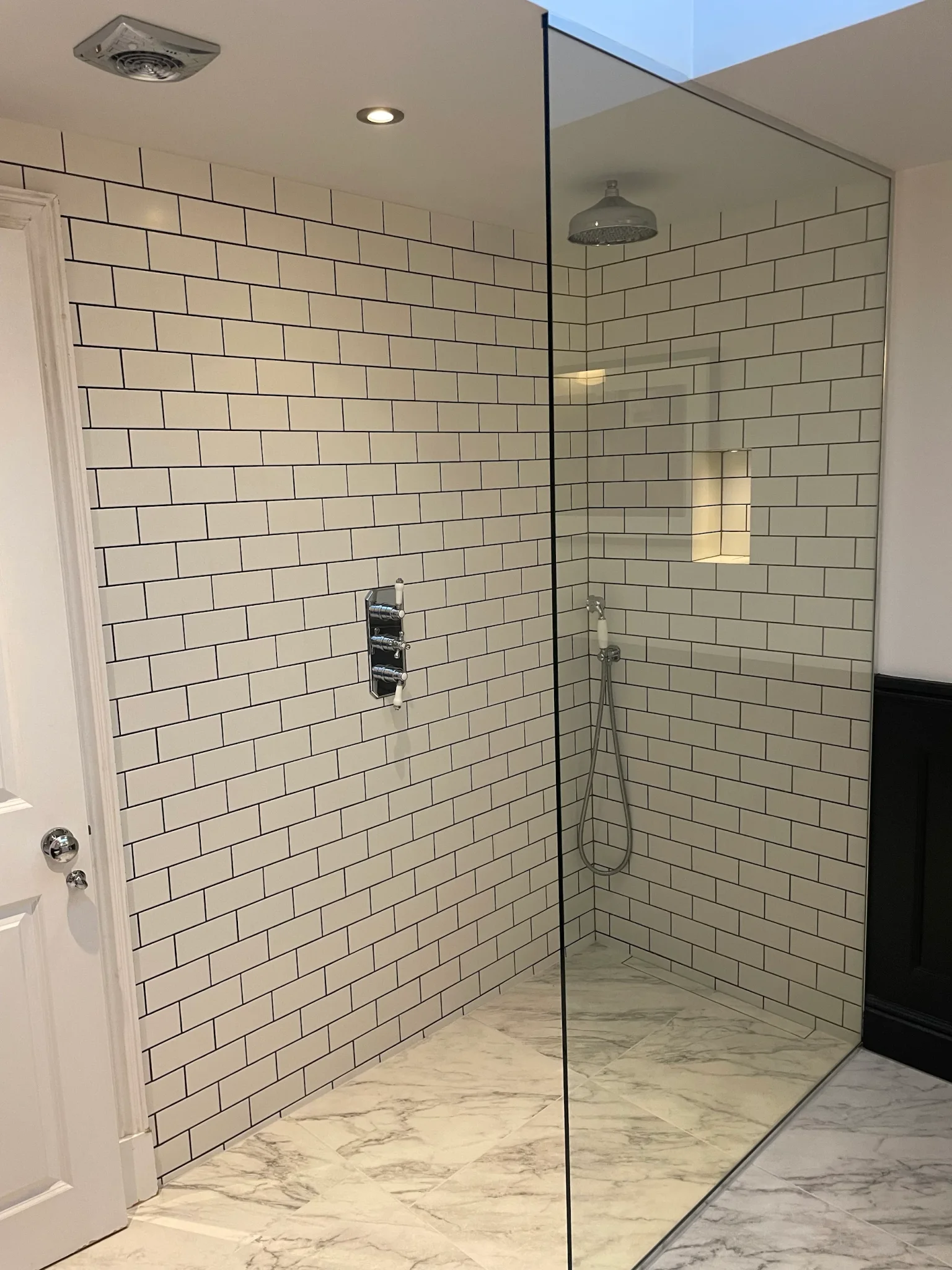 Glass walk-in shower with white metro walls and pale marble-effect floor tiles