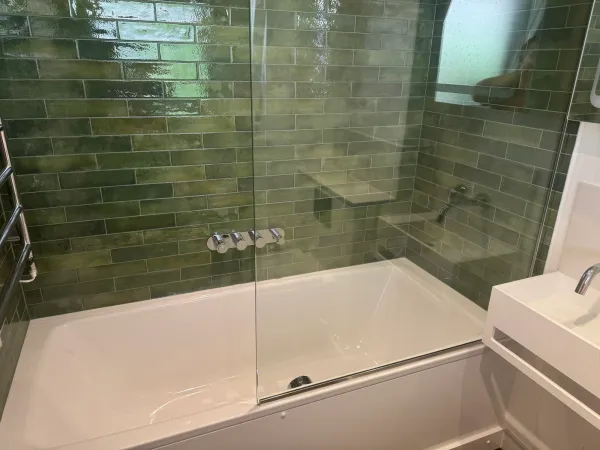 White bath surrounded by glazed green wall tiles