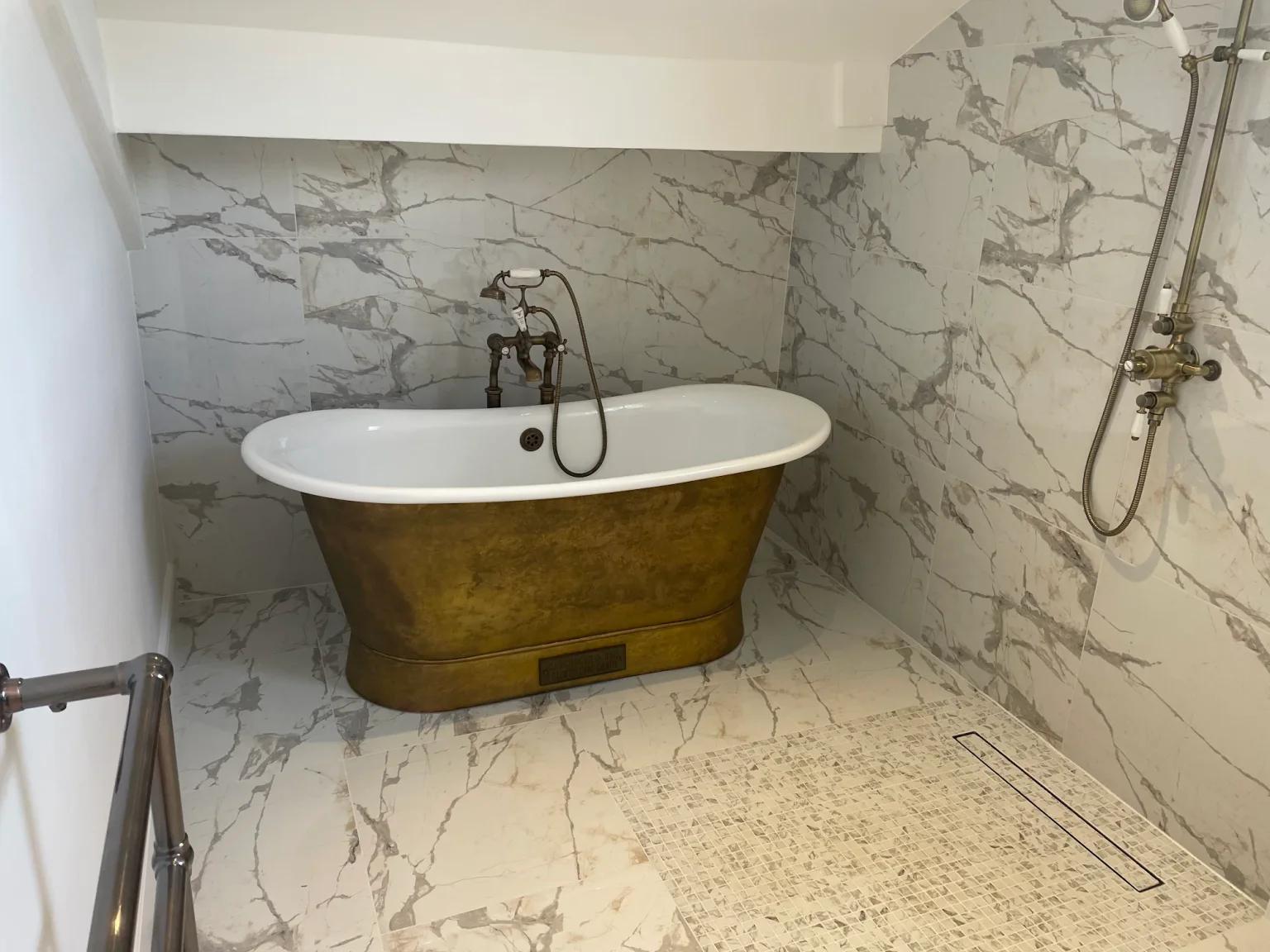 Completed client bathroom with a brass roll-top bath and marble-effect walk-in shower