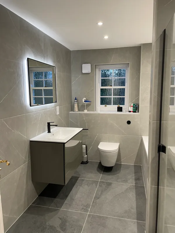 Grey tiled bathroom with black fittings and two windows